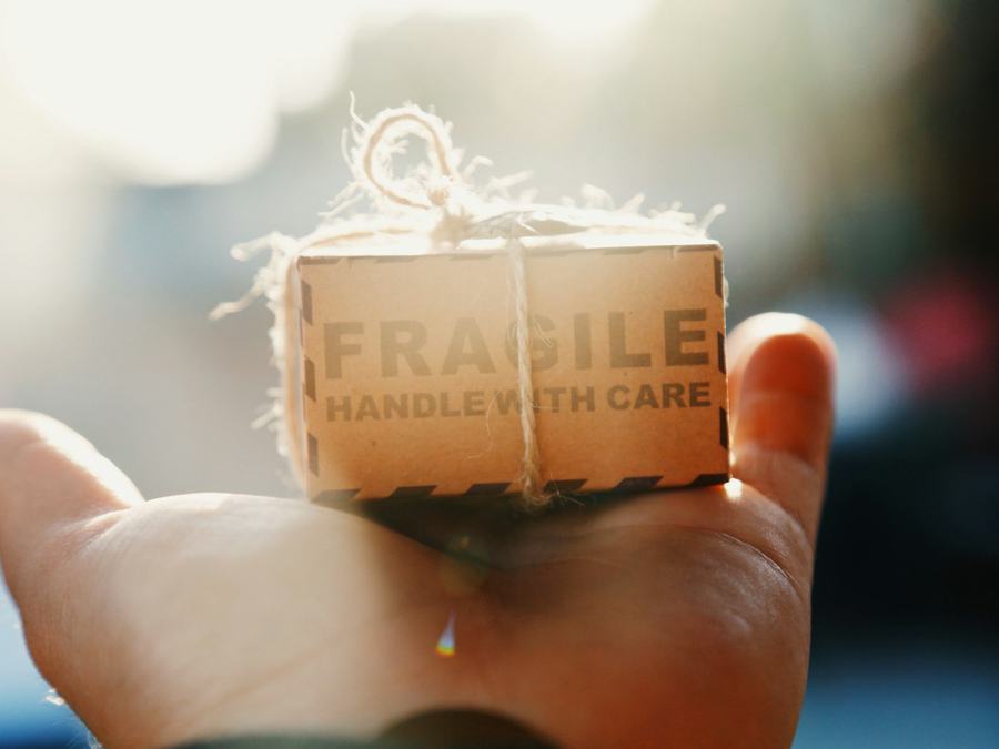 A hand holding a small parcel marked fragile