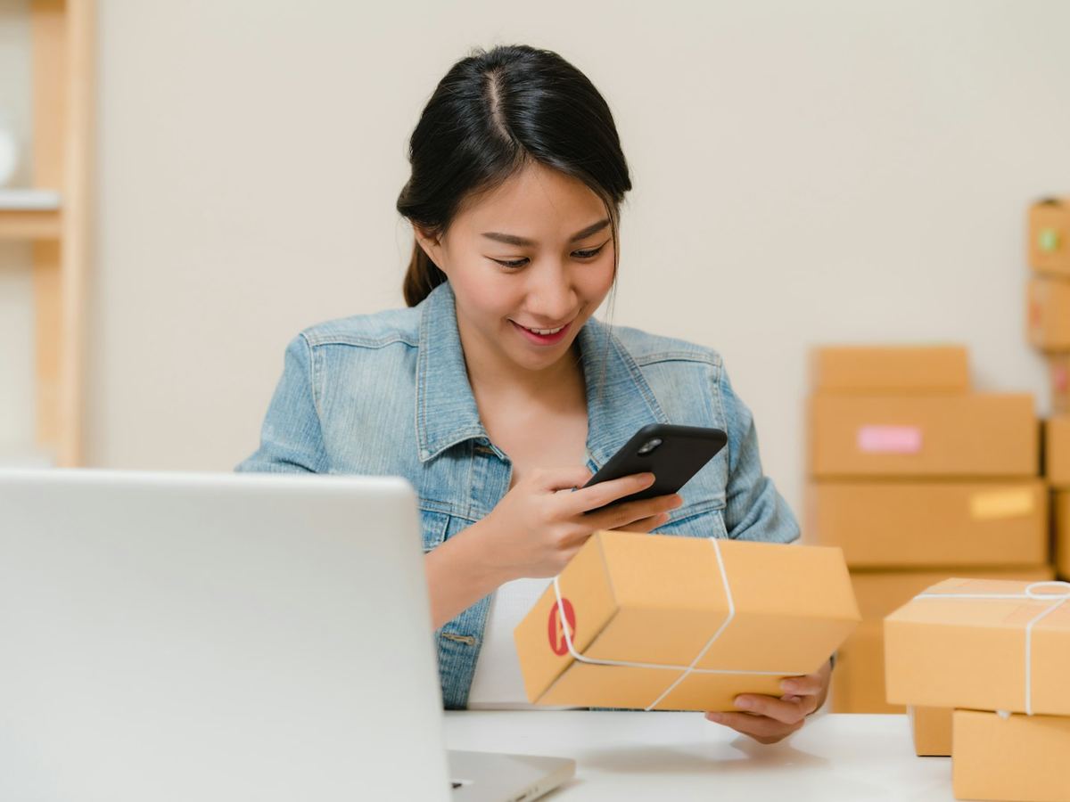 A merchant checking an order on her phone beside packed parcels